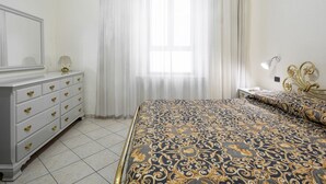 Quarto com cama, penteadeira, mesa de cabeceira, luminária e janela com cortinas.