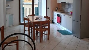 Cozinha compacta com área de refeições, geladeira e televisão na parede.
