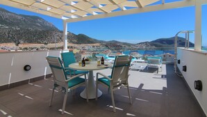 En terrass med ett bord och stolar, utsikt över havet och bergen samt en pergola ovanför.