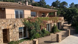 Une maison à deux étages avec des murs en pierre, une terrasse en bois et un escalier en pierre menant à un balcon.