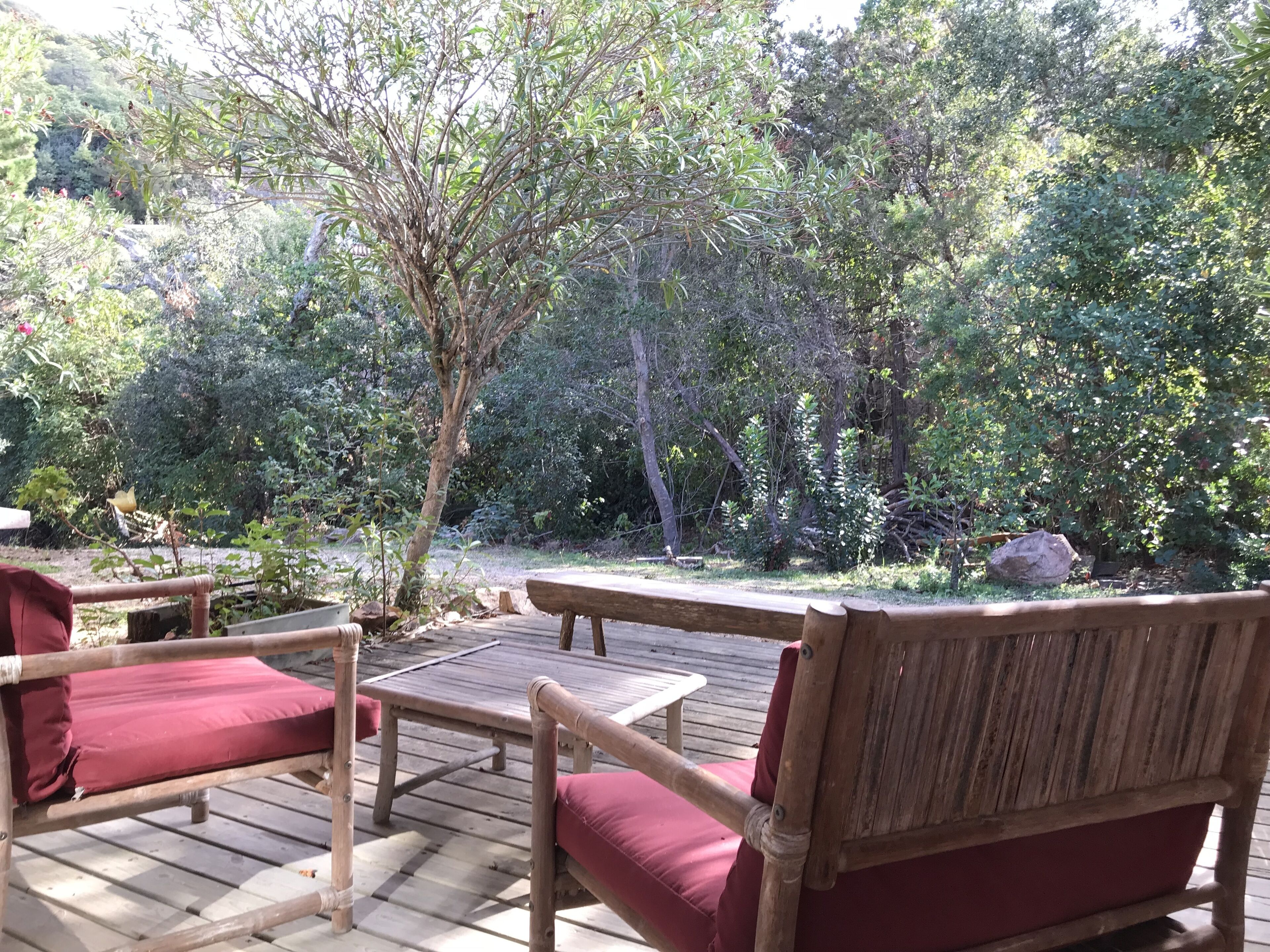 Een houten terras met een tafel en twee stoelen, omringd door weelderige begroeiing en bomen.