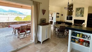 Un vaste espace de vie comprenant un patio, une table à manger et un coin cuisine avec un comptoir et des étagères.