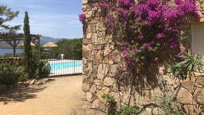 Un mur de pierre orné de fleurs de bougainvillier violettes, une piscine et une vue sur les montagnes.