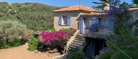 A stone house with a tiled roof, a small front porch, and a gravel driveway.