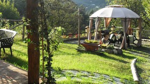 Ein Gartenpavillon mit Tisch und Stühlen, umgeben von einem grünen Garten mit Blick auf Hügel im Hintergrund.