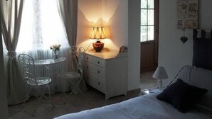 Ein Schlafzimmer mit einem Bett, einem Schreibtisch mit Lampe, einem Stuhl und einem Fenster mit Vorhängen.