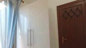 Ein Zimmer mit einem weißen Kleiderschrank, einer Holztür und einem Vorhang.