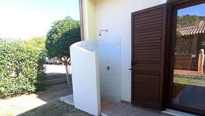 Ein modernes Gebäude mit einer überdachten Außendusche, einer gepflasterten Terrasse und einer Holztür.