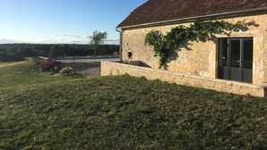Um edifício rústico de pedra com telhado de telhas, um pequeno jardim e vista desobstruída da paisagem circundante.