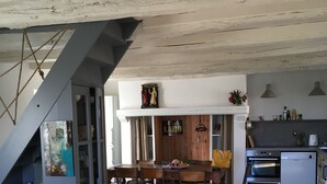 Uma sala de estar moderna com um sofá amarelo, uma área de jantar com mesa e cadeiras de madeira, e uma cozinha com fogão e armários.