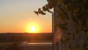 Vista do pôr do sol a partir de uma varanda com grade de metal, parede de concreto e portão.