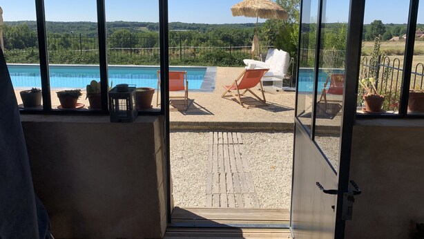 Varanda envidraçada com piscina, móveis de exterior e plantas em vasos.