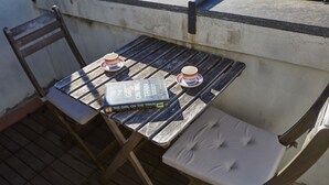 Une petite table d’extérieur sur laquelle se trouve un livre intitulé « La Fille du train » de Paula Hawkins, deux tasses et une chaise avec un siège rembourré.