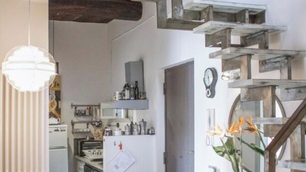 A kitchen with a wooden staircase, a dining table with chairs, and a hanging light fixture.