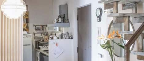 Una cocina con una escalera de madera, una mesa de comedor con sillas y una lámpara colgante.