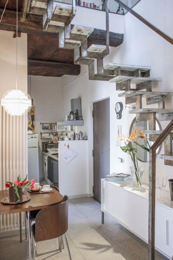 Una cocina con una escalera de madera, una mesa de comedor con sillas y una lámpara colgante.