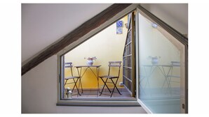 Ein kleiner Balkon mit Tisch und Stühlen, einem Blumentopf und einem Fenster mit Blick ins Freie.