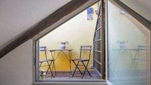 A small balcony with a table and chairs, a potted plant, and a window with a view of the outside.