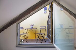 Un pequeño balcón con una mesa, sillas, una planta en maceta y una ventana con vistas al exterior.