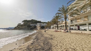 Una spiaggia con una riva sabbiosa, palme e un edificio con balconi che si affacciano sul mare.