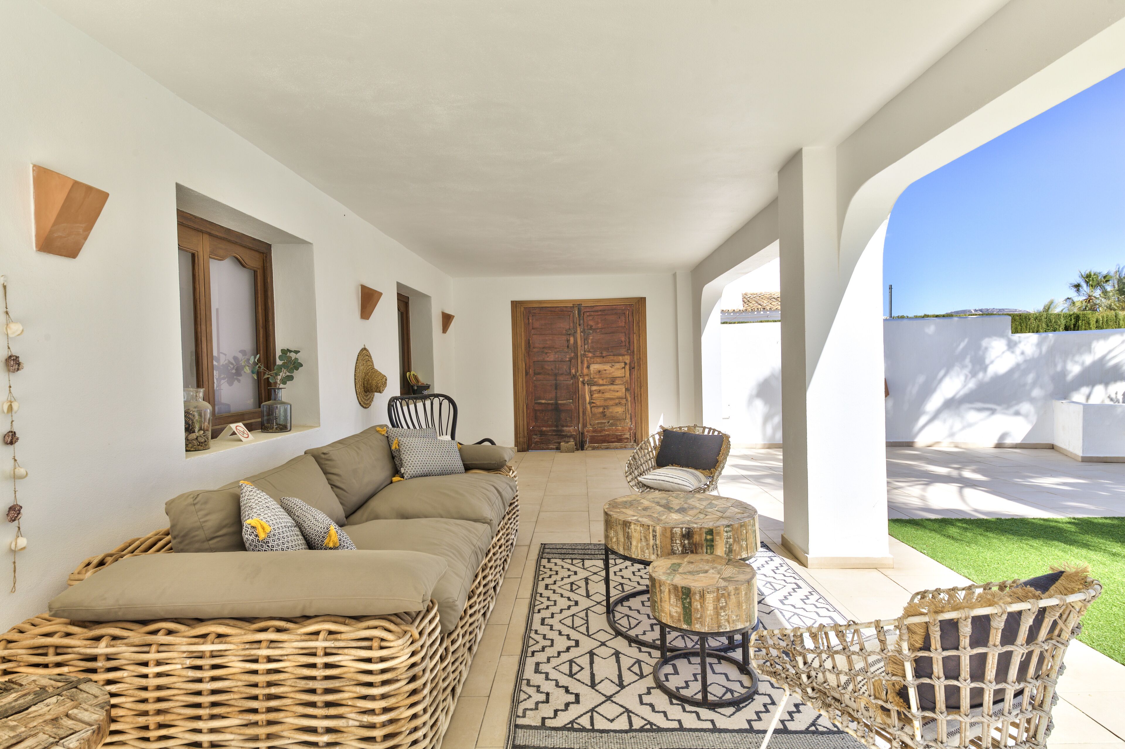 Un'ampia zona giorno con un divano in vimini, tavolini rotondi e vista su un giardino rigoglioso.
