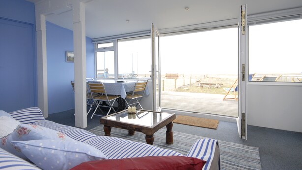 A room with a bed, a table, and a view of the beach through large windows. - Beach Retreat - the perfect seaside escape. (Seasalter)