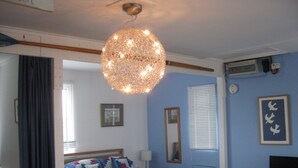 A bedroom with a bed, a hanging light fixture, a television on a stand, and a window with blinds. - Beach Retreat - the perfect seaside escape. (Seasalter)