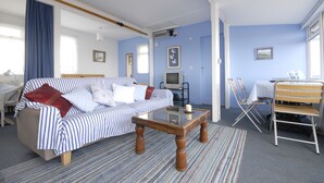 A living room with a striped sofa, a wooden coffee table, and a dining area with metal chairs and a table. - Beach Retreat - the perfect seaside escape. (Seasalter)