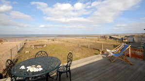 A deck with a table and chairs overlooking a beach. - Beach Retreat - the perfect seaside escape. (Seasalter)