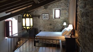 Une chambre avec un mur en pierre, un lit, une table de chevet avec une lampe, un escalier en bois et un luminaire suspendu.