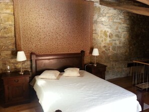A bedroom with a wooden headboard, two bedside tables with lamps, a bed with white bedding, and stone walls. - Charming house inside walls of Óbidos (Óbidos)