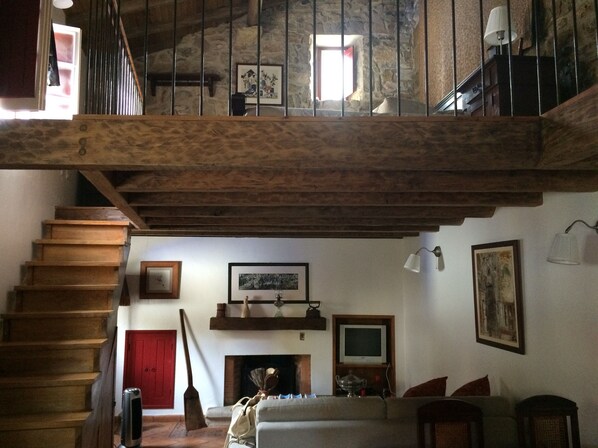 A rustic interior with a wooden staircase, a fireplace, a sofa, and a television.