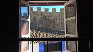 Une fenêtre ouverte donnant sur un mur de pierre et un toit recouvert de tuiles.