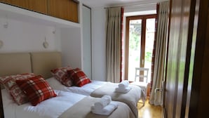 Habitación de hotel con dos camas, cada una con almohadas rojas y blancas, y una pequeña silla junto a la ventana.