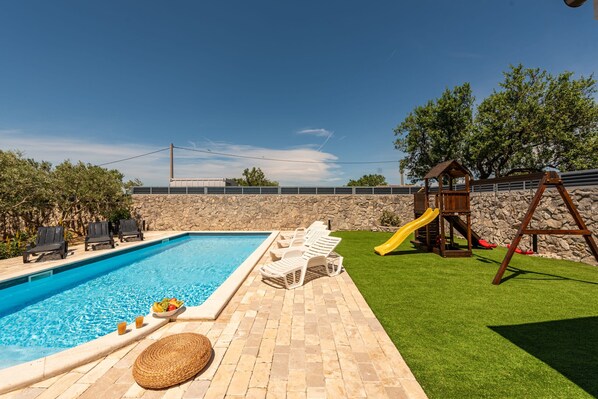 A swimming pool with lounge chairs, a children's play area, and a stone wall. - Villa Elder ZadarVillas (Lepuri)