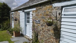 Ett stenhus med en vit dörr, en skylt med texten ”Dozmary Cottage” och hängande blomkorgar.