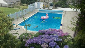 En swimmingpool med en rosa uppblåsbar flamingofigur, omgiven av en byggnad i sten och frodig grönska.