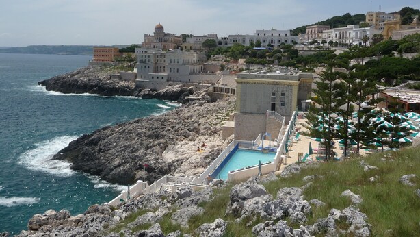 Ein Küstenhotel mit Pool, felsigem Gelände und Gebäuden im Hintergrund.