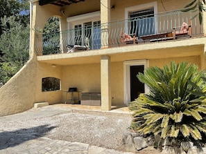 A two-story building with a balcony, a door, and a small table with a chair.