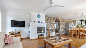 A living room with a fireplace, a television, a stone wall, and a dining area with wooden furniture. - Jasmine Padre Aviles 17th C converted convent with pool, tennis & amazing views (Malaga)