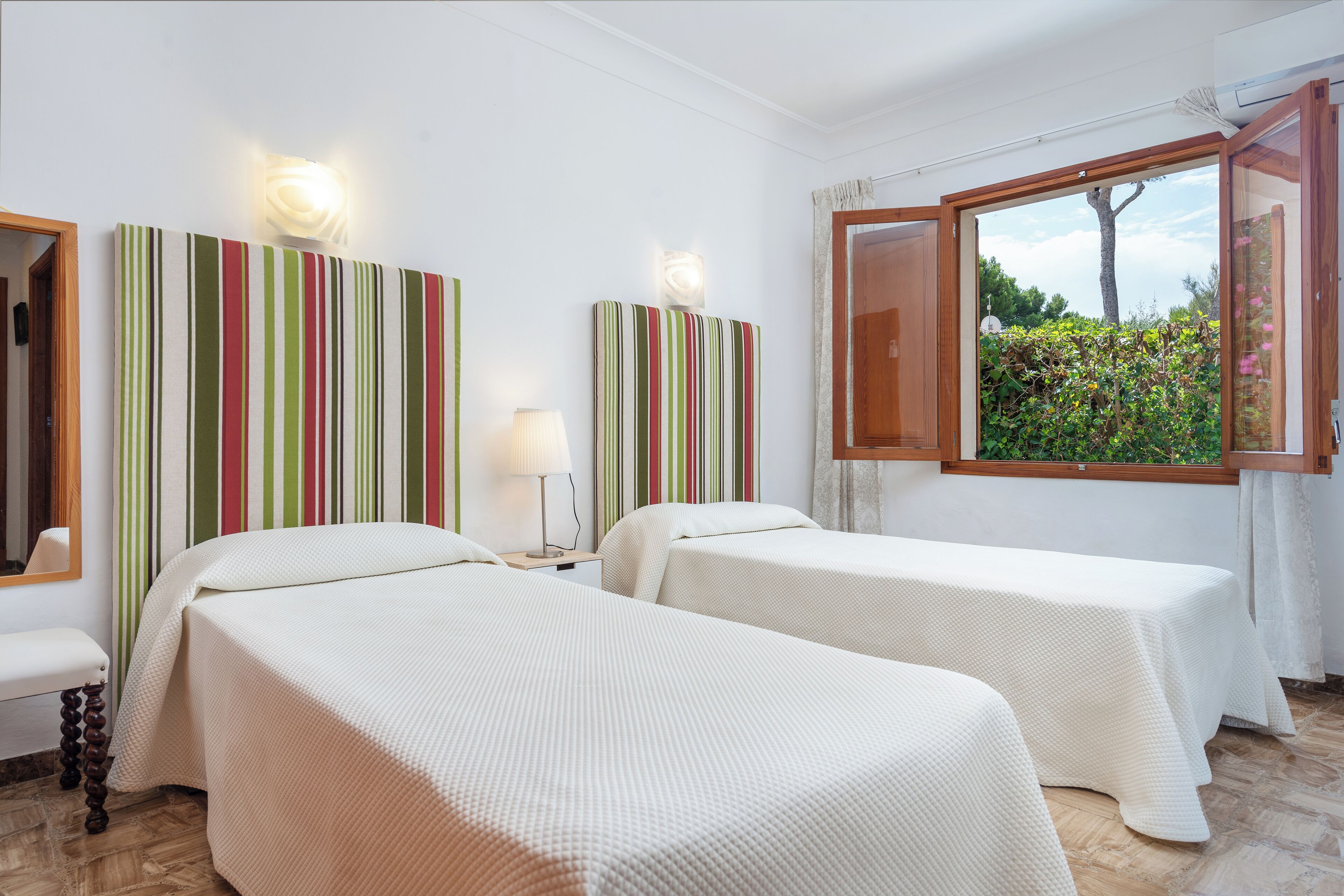 A hotel room with two beds, a large window with a view of greenery, and striped wall art.