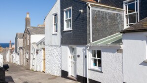 Une rangée de charmantes maisons de bord de mer aux murs blancs et aux toits sombres, une rue étroite et, au loin, une vue dégagée sur la mer.