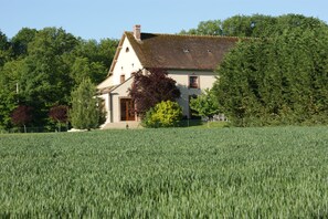 Una casa con techo inclinado, rodeada por un campo y árboles.