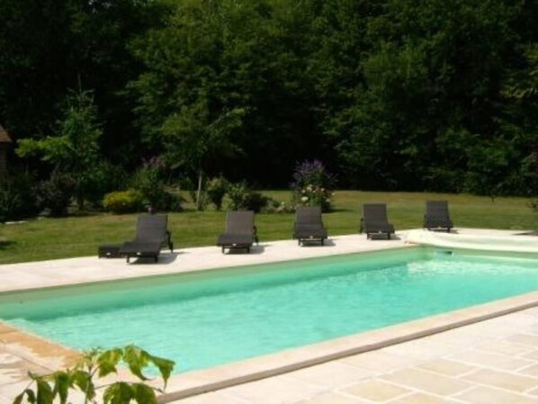 Une piscine avec des chaises longues et un espace jardin.