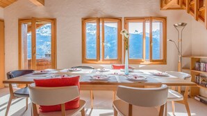 A dining area with a table set for four, large windows with mountain views, and a bookshelf with books.