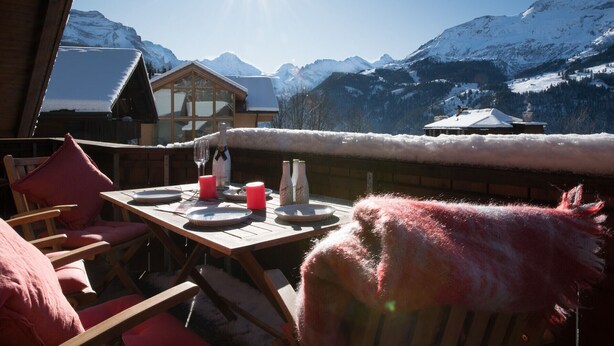 A wooden table with plates, glasses, and bottles, set against a snowy mountain backdrop.