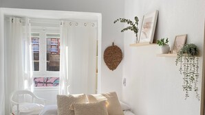 A bedroom with a bed, a ceiling fan, a window with curtains, a chair, and wall decorations including a hanging plant and framed pictures. - Apartment on the Beach Malvarrosa Cabañal, CA MICAELA- Wifi free, easy parking (València)