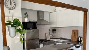 A kitchen with a brick backsplash, stainless steel appliances, a hanging clock, and a bar area with stools. - Apartment on the Beach Malvarrosa Cabañal, CA MICAELA- Wifi free, easy parking (València)