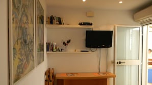 Quarto com cama, escrivaninha, televisão e porta para uma varanda.
