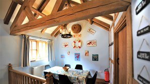 A dining area with a table set for two, wooden beams above, and various wall decorations including a life preserver and a fish. - Lobster Pot in Padstow Is A 'fisherman's Style' Cottage With A Parking Space. (Padstow)
